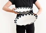 A person holding a Black Arabesque Scallop 11 Pasta Bowl, showcasing a black arabesque pattern on a white base. Perfect for serving and as stylish décor.