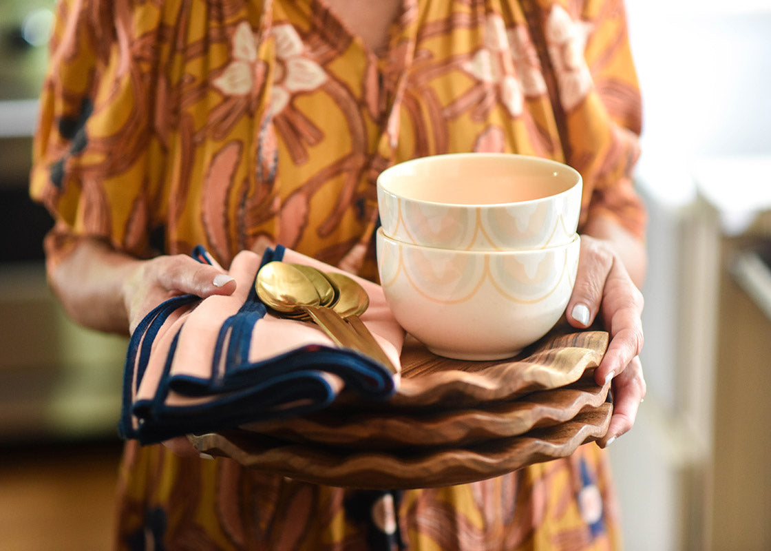 Front View of Woman holding stack of Fundamental Wood Ruffle Dinner Plates and Napkins