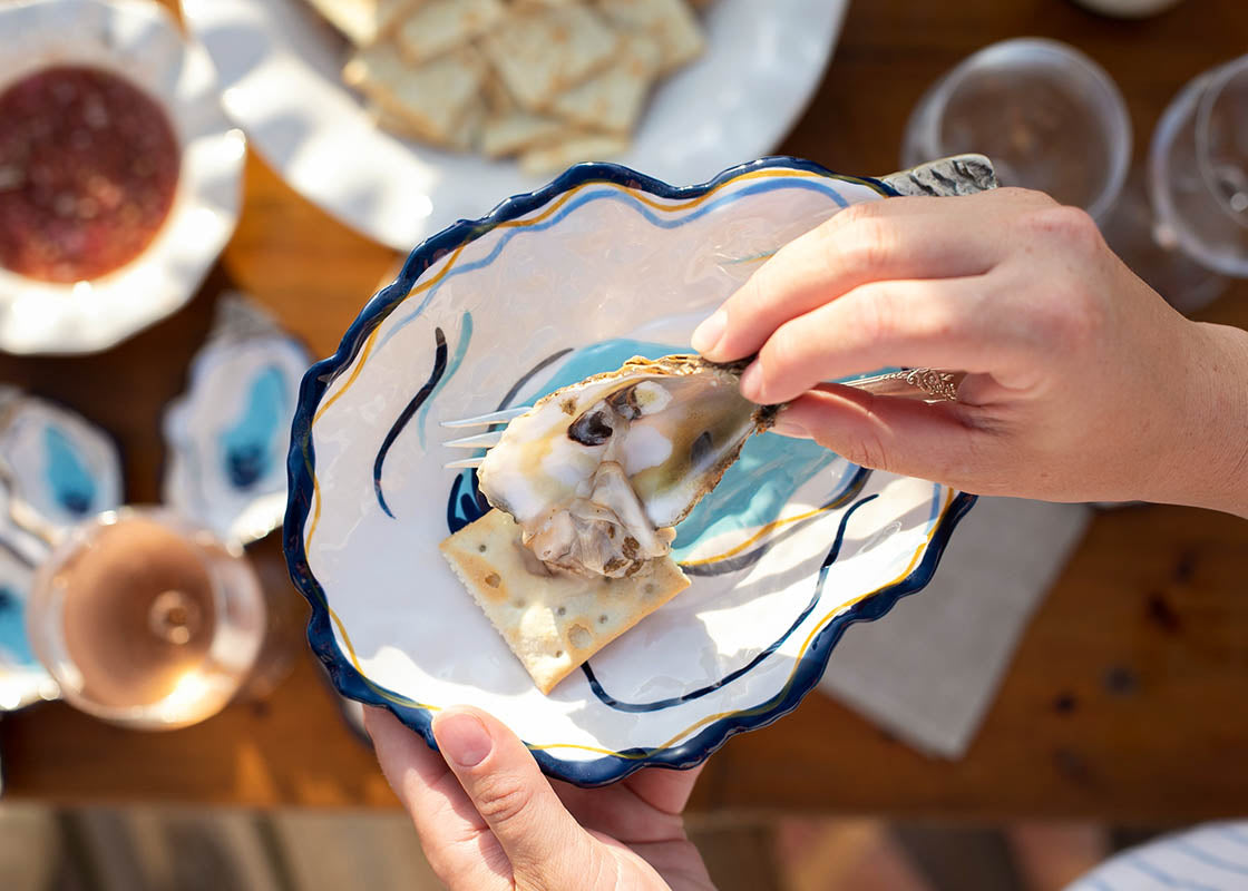 Overhead View of Person Holding Functional Oyster Plate with One Hand and Putting Oyster on Cracker