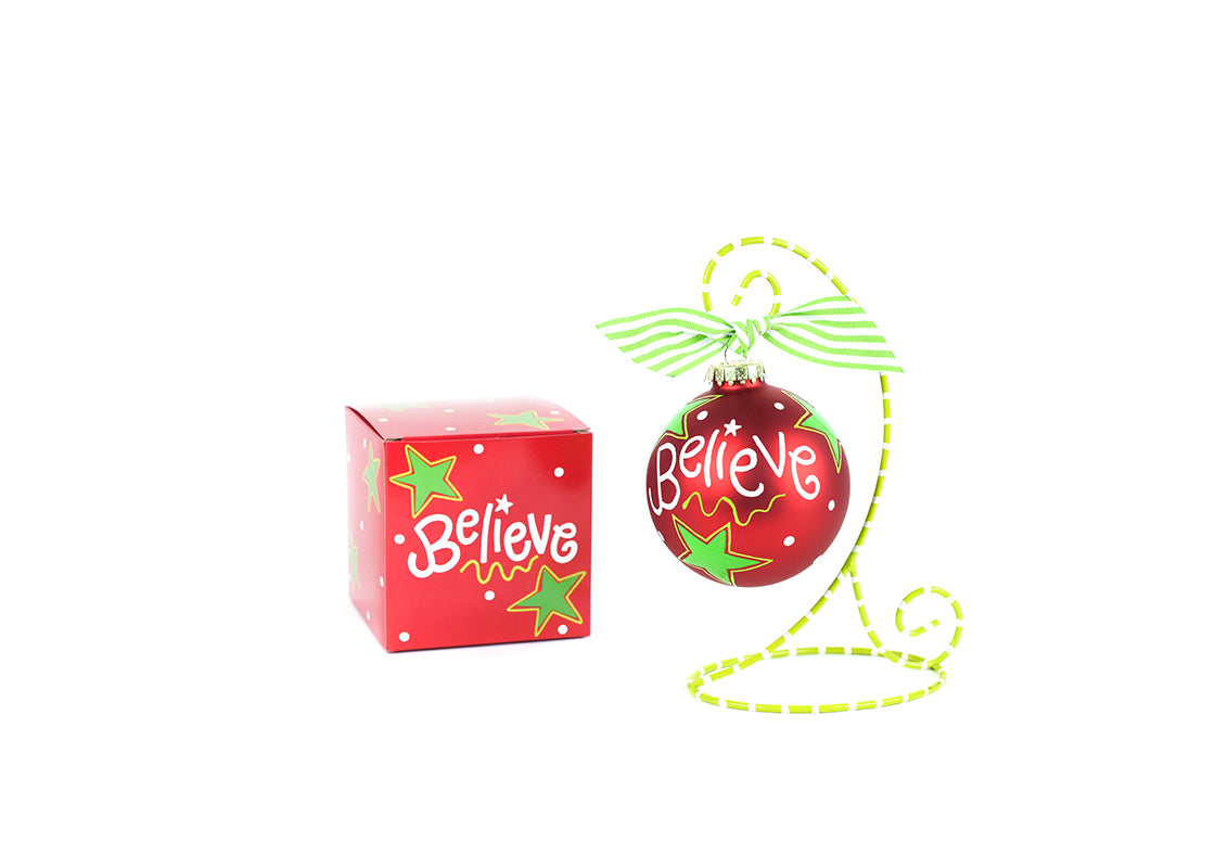 Front View of Believe Christmas Glass Ornament Placed on Green Display Stand and Matching Box