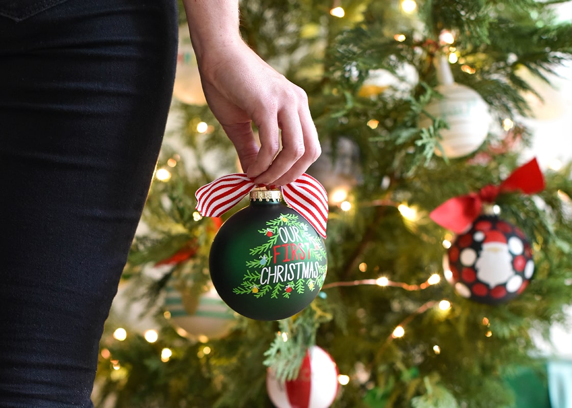 Front View of Person Holding to her Side Our First Christmas Ornament Looking for the Perfect Spot to Place on Christmas Tree