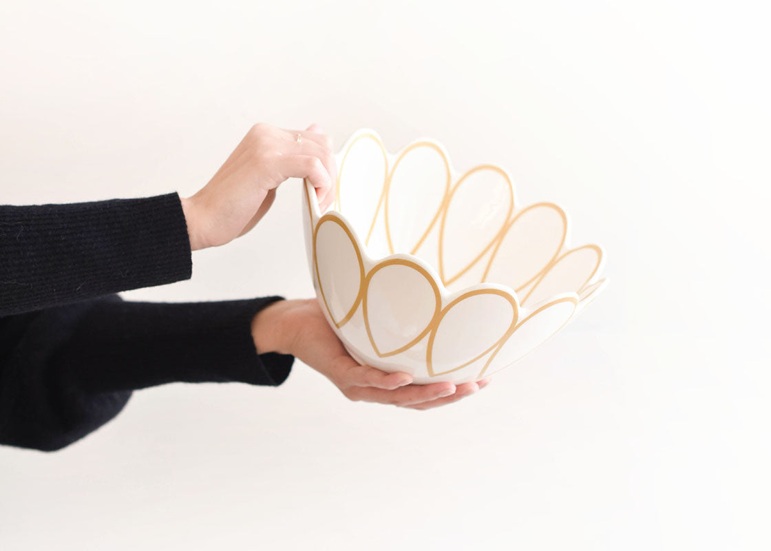 Front View of Woman Holding Deco Gold Scallop Serving Bowl Tipped to Side Featuring the Design Details on Scalloped Edge