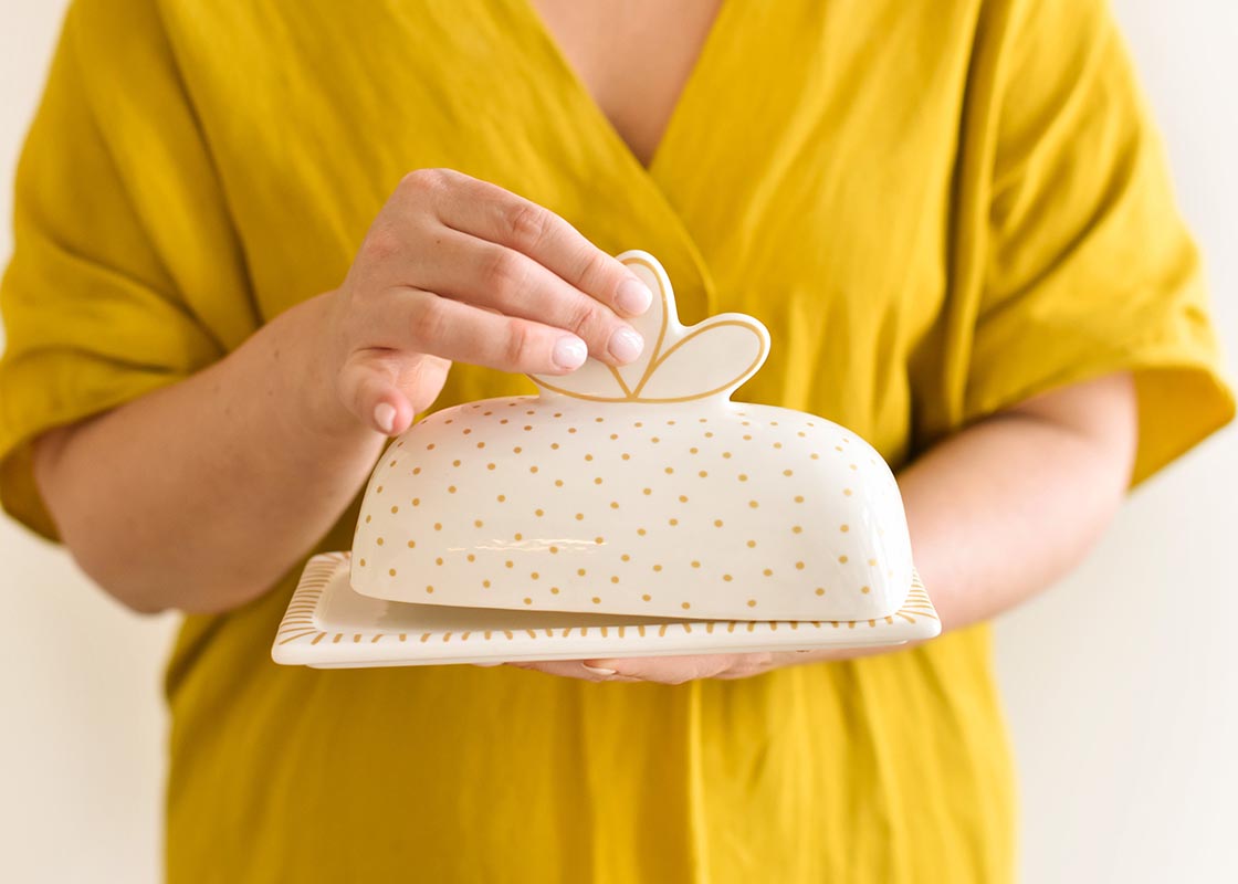 Front View of Woman Holding Deco Gold Scallop Knob Butter Dish and Lifting Lid by Scallop Knob