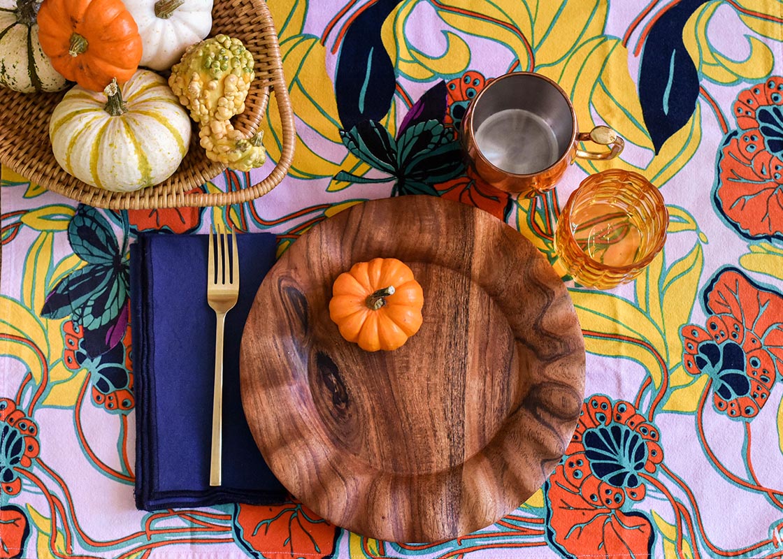 Overhead View of Simple Place Setting with Fundamental Wood Ruffle Dinner Plate Set on a Colorful Tablecloth and Colorful Pumpkins