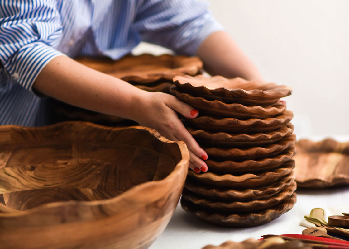 Front View of Woman Placing a Stack of Ruffle Wood Salad Plates onto Table with Coordinating Fundamentals Collection Designs