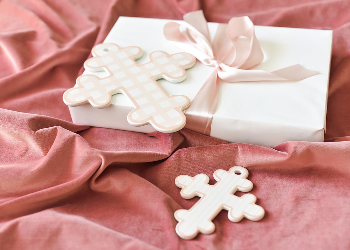 Cropped View of Ceramic Crosses Including 10in Pink Gingham Cross Placed on Wrapped Gift