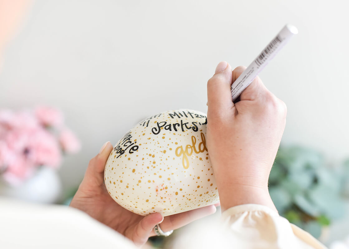 Front View of Hand with Personalizing Pen Writing the Names of the Annual Winner of the Hunt onto Speckled Golden Egg Capturing the Memory