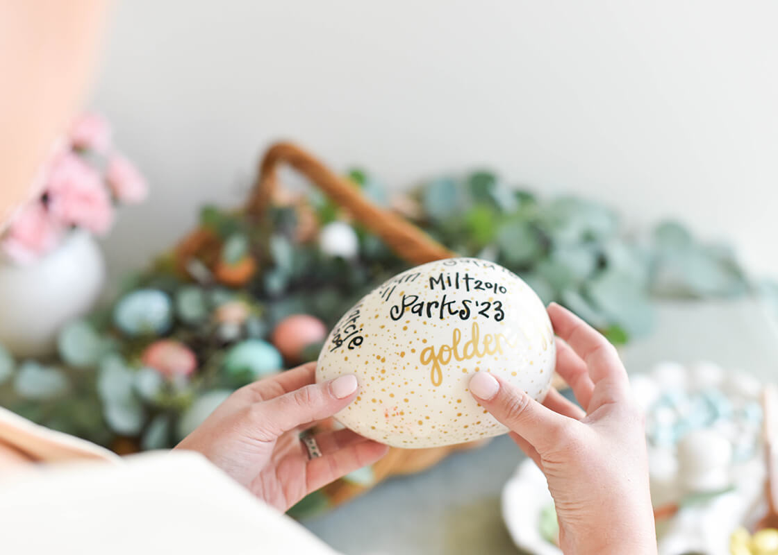 Cropped Close up of Woman Holding Speckled Golden Egg with Writing Capturing the Egg Hunt Winner's Names