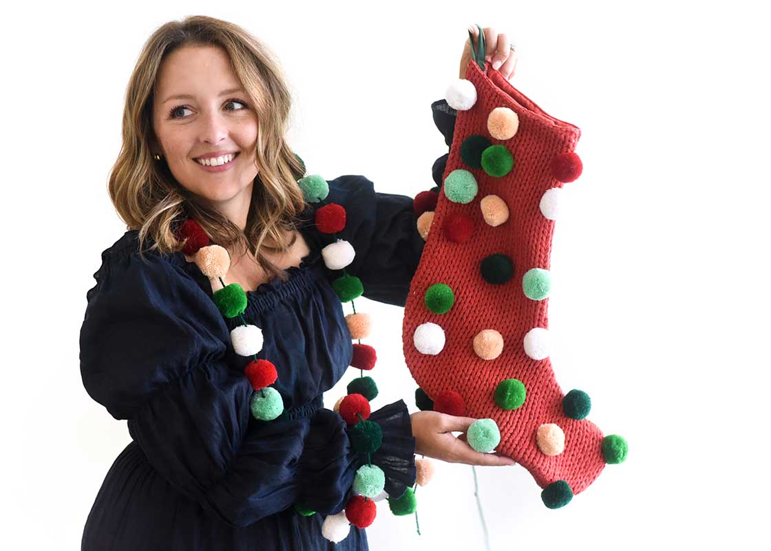 Close up of Woman Holding up Red Pom Pom Stocking with Coordinated Pom Pom Garland Draped Around Shoulders