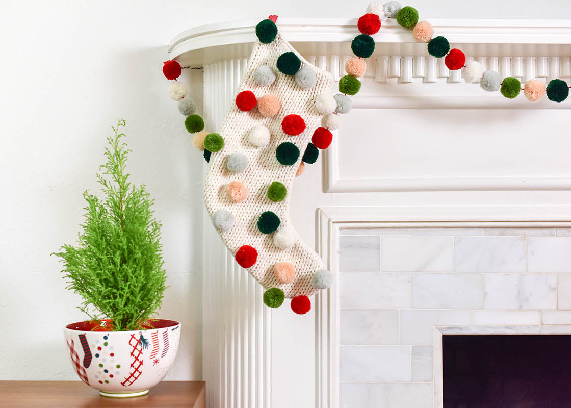 Front View of Christmas Knit Stocking with Pom Poms and Coordinating Pom Pom Garland on Mantle