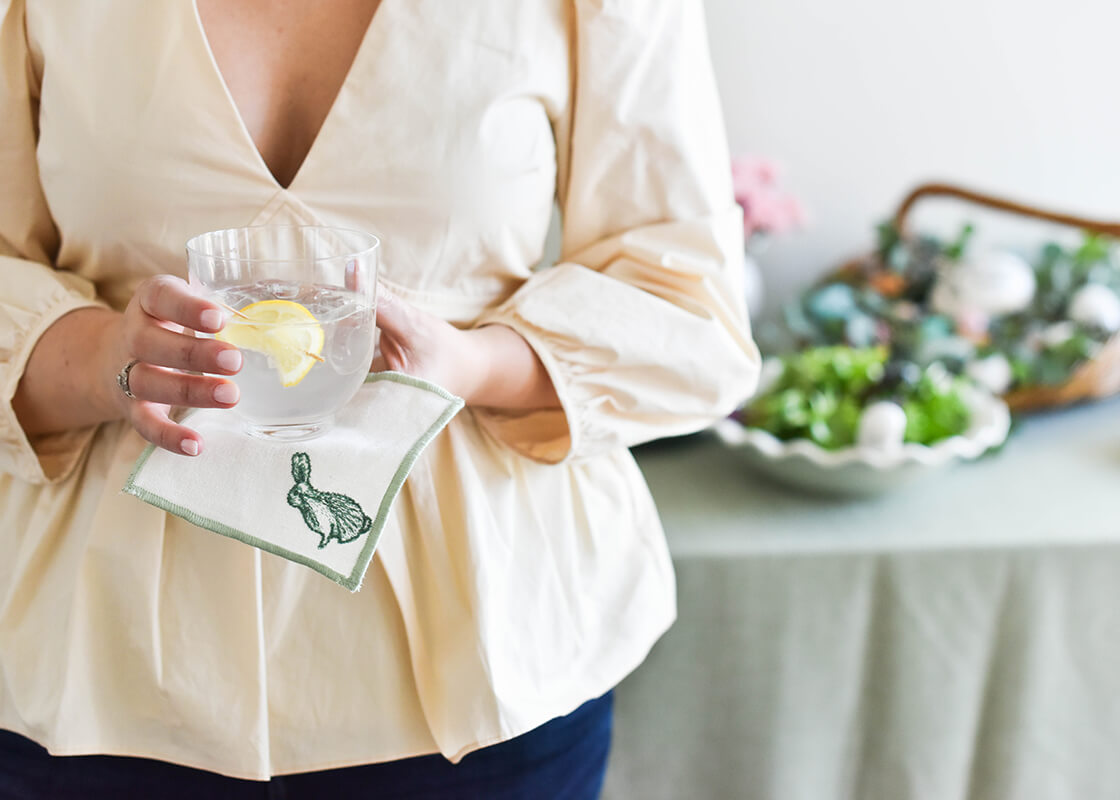 Front View of Woman Holding Cocktail and Speckled Rabbit Cocktail Napkin from the Set of 4