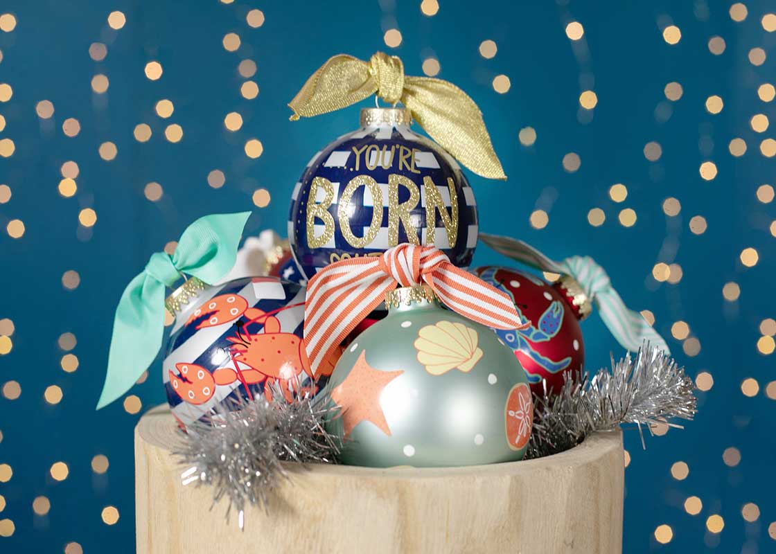 Cropped View of Coton Colors Glass Ornaments Including Shells Design with Twinkle Lights in Background