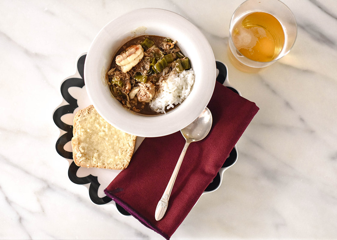 Overhead View of Individual Place Setting with Black Arabesque Trim Scallop Dinner Plate and Coordinating Bowl Serving Gumbo