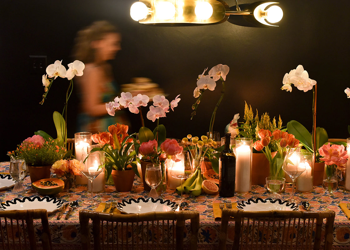 Side View of Candlelit Tablescape Including Black Arabesque Scallop Dinnerware 12 Piece Set with Woman Walking Behind Holding a Platter