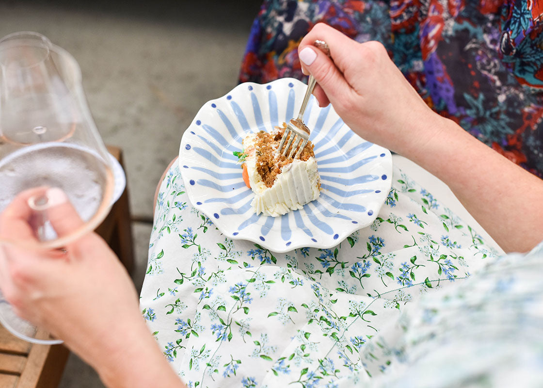 Overhead View of Seated Woman with Iris Blue Burst Ruffle Salad Plate in Lap Holding a Fork in her Right Hand and a Wine Glass in her Left