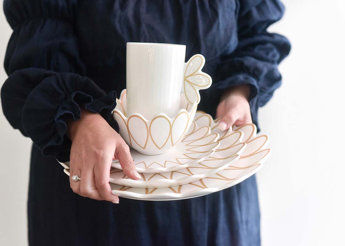 Front View of Woman in Navy Dress Holding Deco Gold Scallop Platter with Coordinating Pieces Stacked on Top