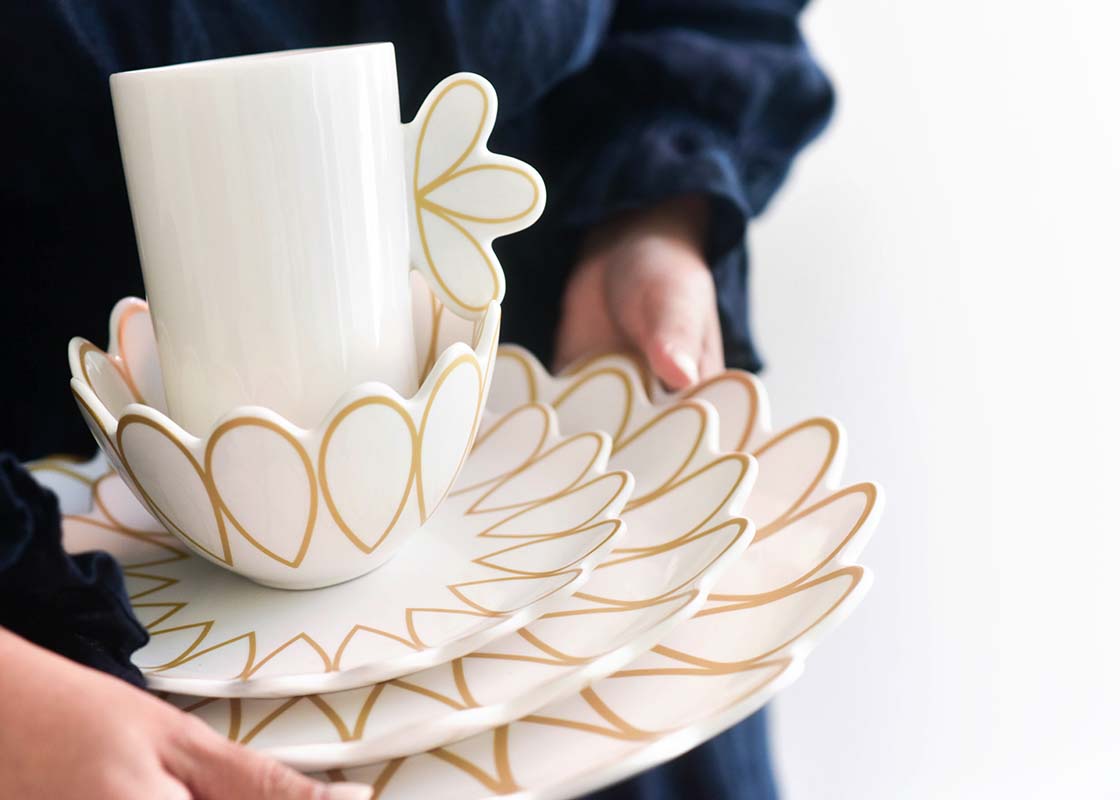 Front View of Woman Unsteadily Holding a Stacked Deco Gold Scallop 4 Piece Place Setting