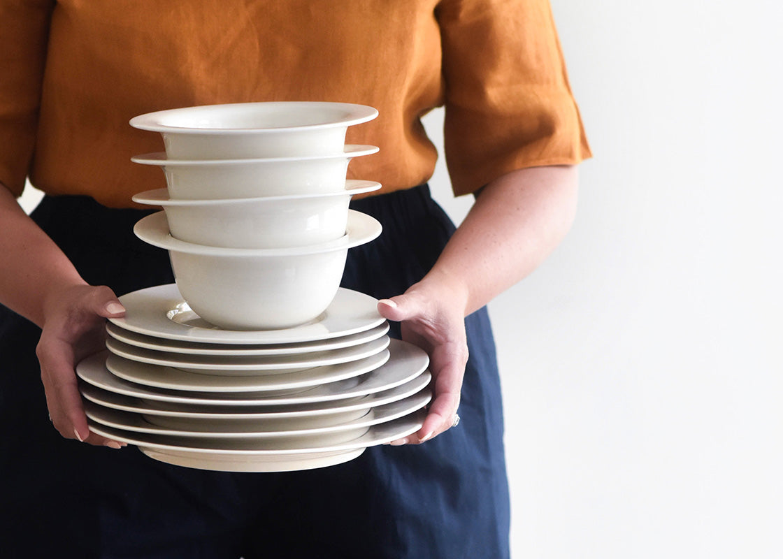 Close up of Woman Holding Neatly Stacked Signature White Rimmed 4 Piece Place Settings