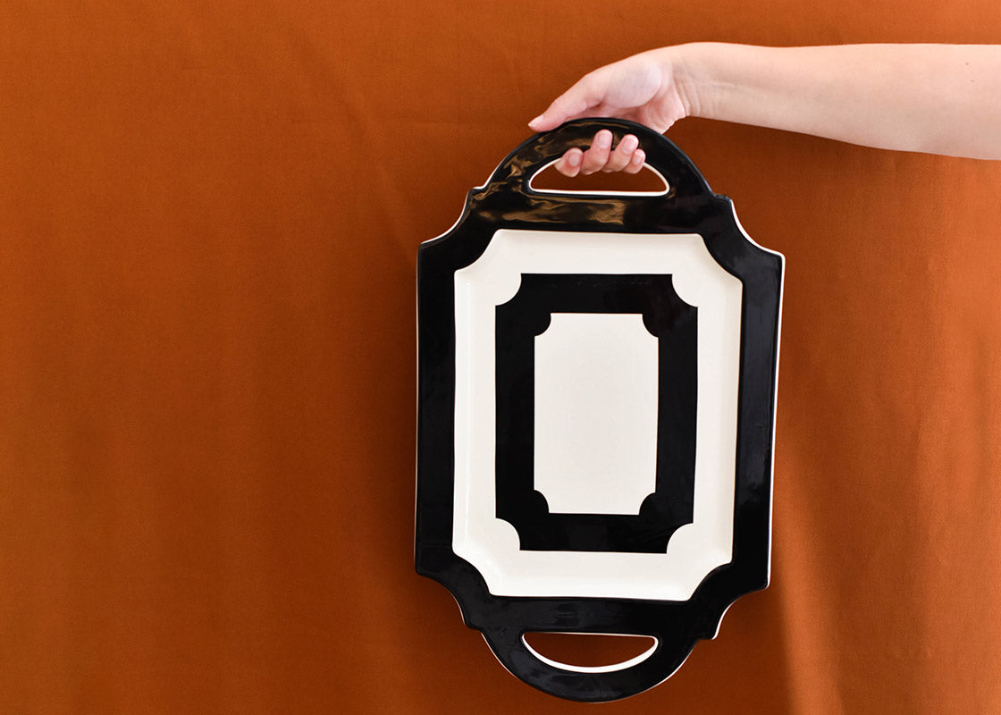 Cropped Close up of a Hand Holding a Deco Traditional Tray by the Pierced Handle Highlighting its Bold Black and White Geometric Pattern