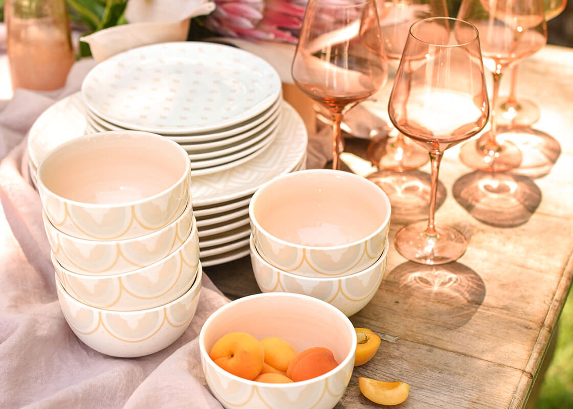 Front View of Stacks of Coordinating Tableware with Small Bowl Blush Arabesque Trim Design Placed on Pine Table