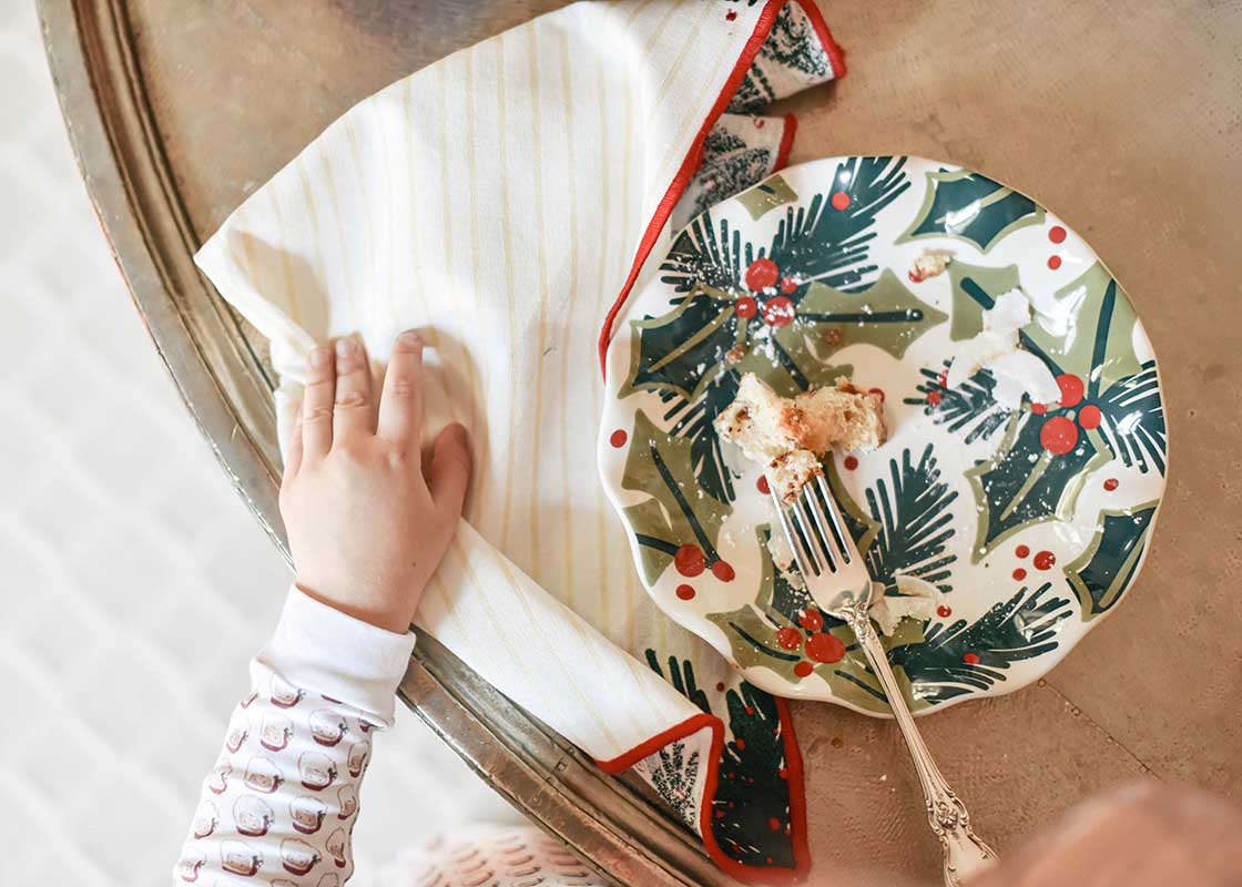 Overhead View of Child's Hand Reaching for Napkin Next to Holly Ruffle Salad Plate