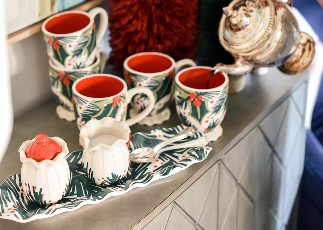 Cropped Close up of Silver Pot Pouring Coffee into Holly Mug set on Balsam Ruffle Skinny Tray Among Stacks of Mugs, Creamer and Sugar Set