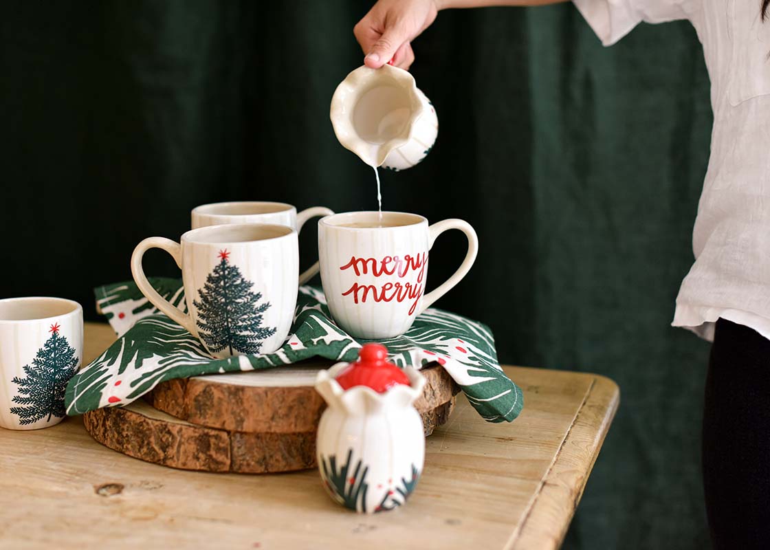 Front View of Woman Pouring Milk into a Balsam and Berry Ruffle Christmas Mug with Coordinating Creamer and Sugar Set