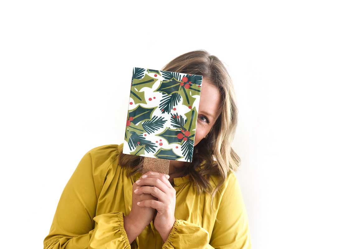 Front View of Woman Peeking Behind Holly Wood Small Rectangle Board She is Holding in Front of Her