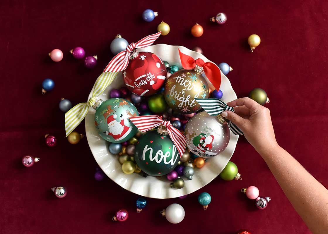 Overhead View of Hand Placing an Ornament into Bowl Filled with Many Ornaments Including Christmas Calling Reindeer Glass Ornament