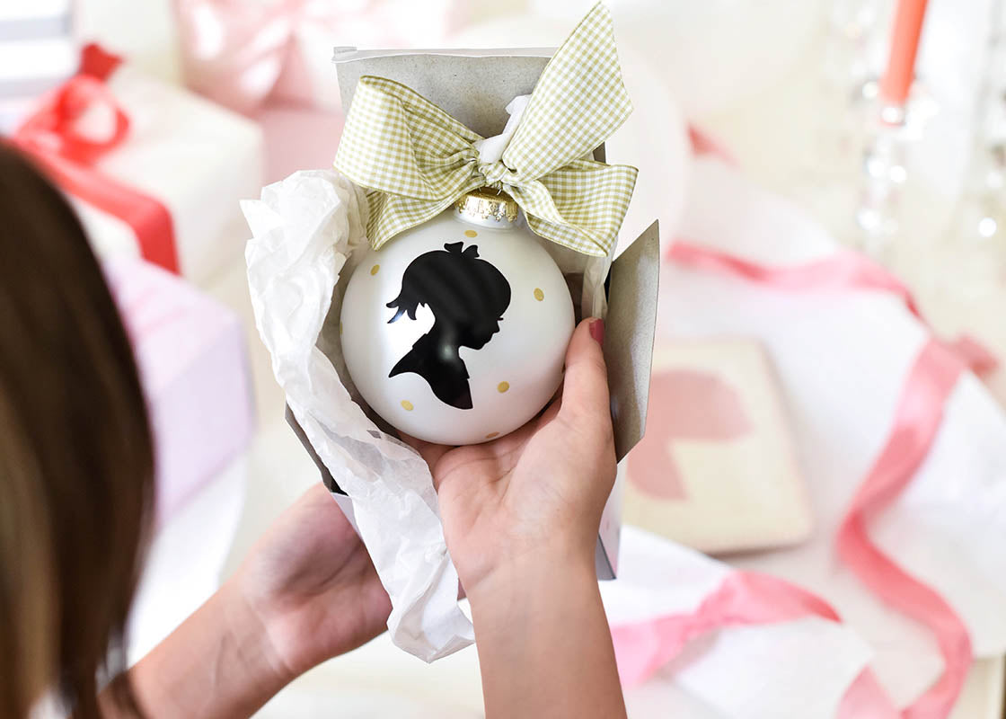 Overhead View of Woman Removing a Girl Silhouette Ornament from Matching Gift Box with Pink and White Wrapped Gifts in Background