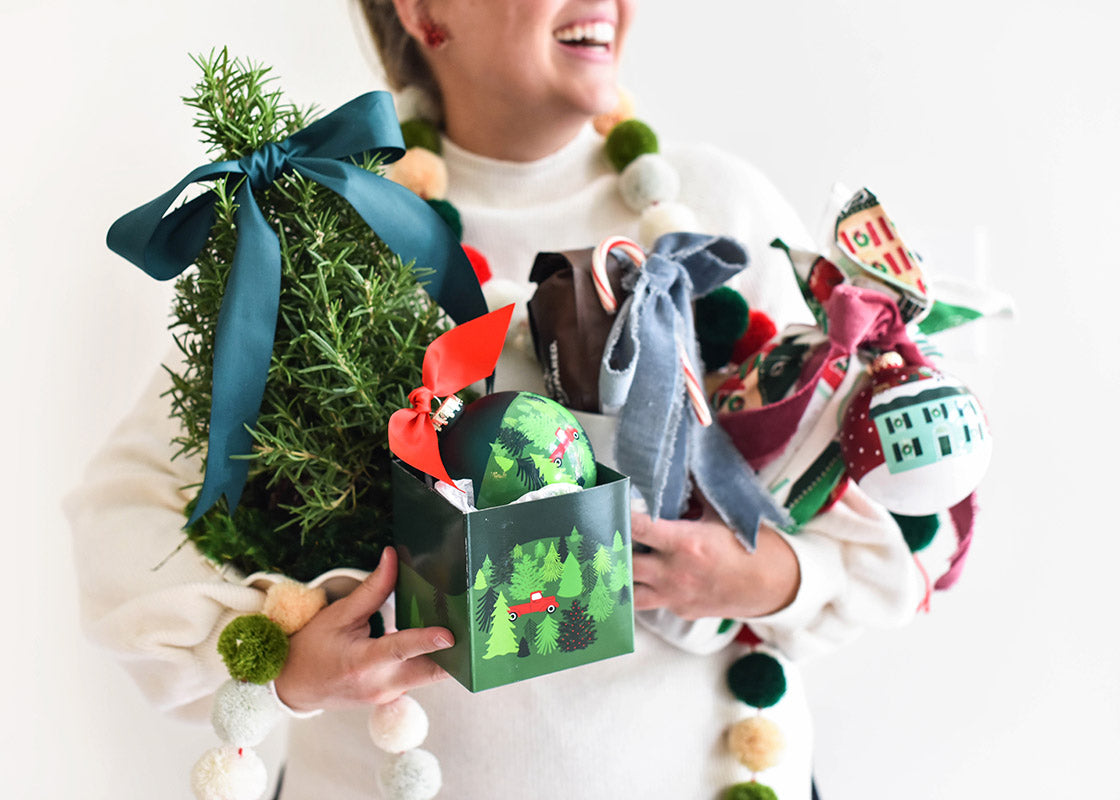 Cropped View of Woman Smiling with Arms Full of Gifts Including a Truck on a Tree Farm Glass Ornament