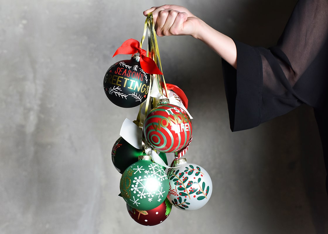 Front View of Person Holding Bundle of Holiday Ornaments Including It’s A Wonderful Life Glass Ornament Tied Together with a Ribbon