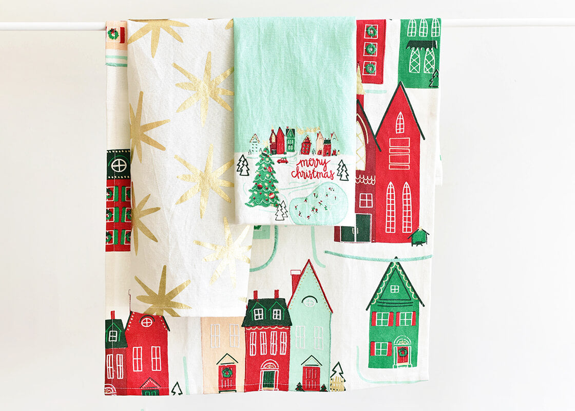 Front View of Folded Coton Colors Holiday Linen Designs Including Christmas Village Homes Layered and Hung on Towel Rod to Inspire