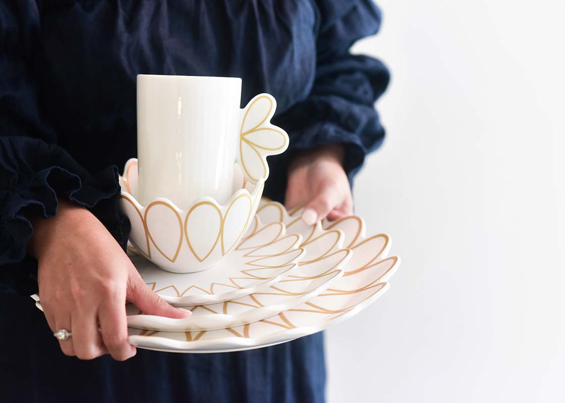 Left Side View of Woman Holding a Stack of Dishes Including Deco Gold Scallop Small Bowl