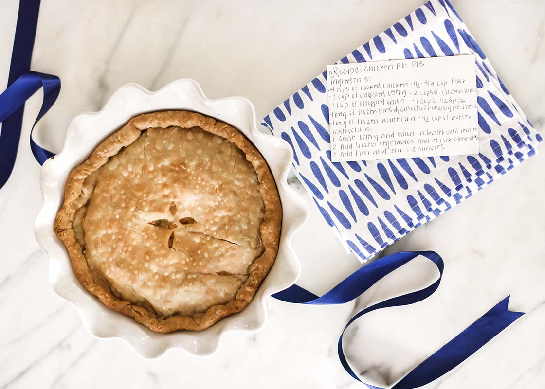 Overhead View of Artfully Designed Kitchen Towel with Iris Blue Drop Design Placed Next to Baked Pie and Recipe Card