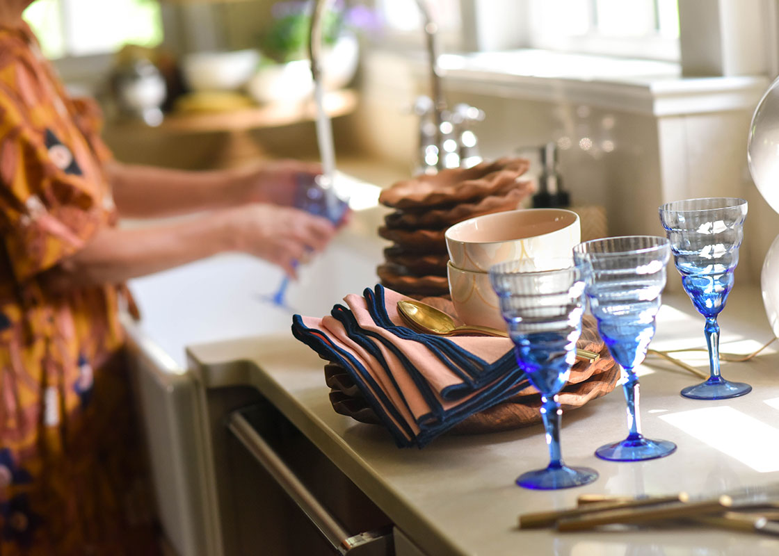 Cropped View of Dinnerware Including Wood Ruffle Dinner Plate and Blue Glasses Being Washed in Kitchen Sink