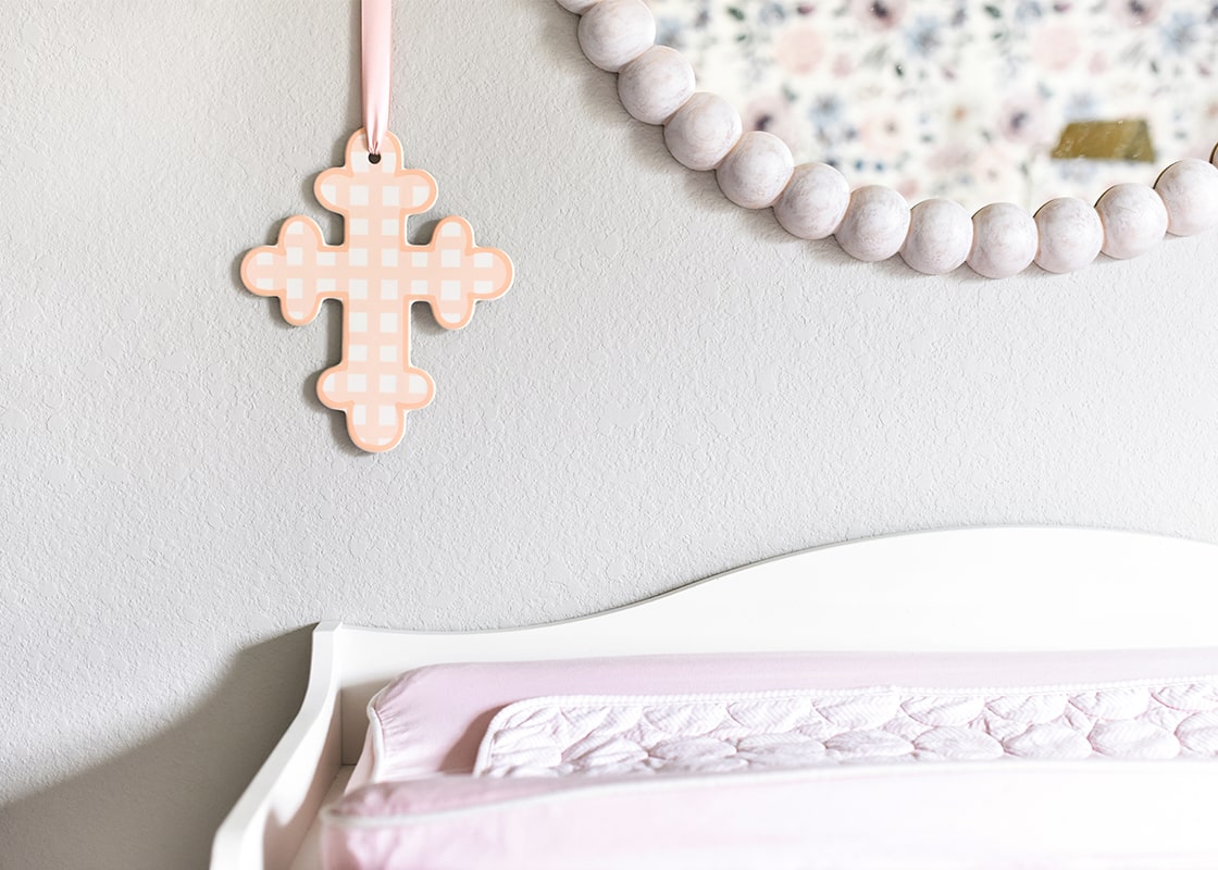 Front View of Ceramic Cross Pink Gingham Design Hanging above Bed by a Pink Ribbon