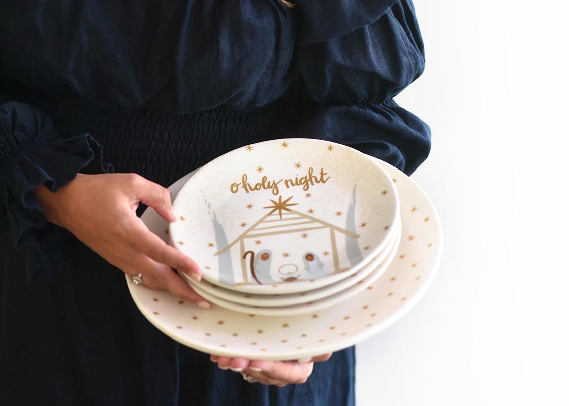 Front View of Woman Holding Stack of Brown Skin Nativity Salad Plates Set atop Star Dinner Plate