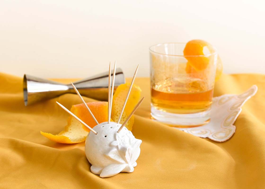 Front View of Shaped Orange Toothpick Holder with Orange Garnish in a Cocktail Glass