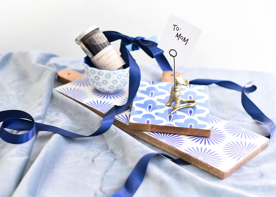 Front View of a Stack of Iris Blue Boards and Appetizer Bowl set on Wrapping Paper and Ribbon Ready to be Wrapped for Gifting to Mom