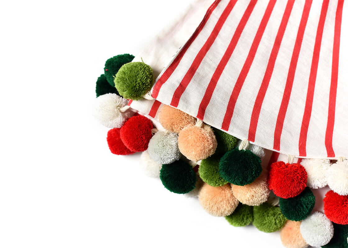 Cropped Close up of Folded Red Stripe Tree Skirt with Pom Poms Showcasing Colorful Pom Pom Trim and Beautiful Texture of Fabric