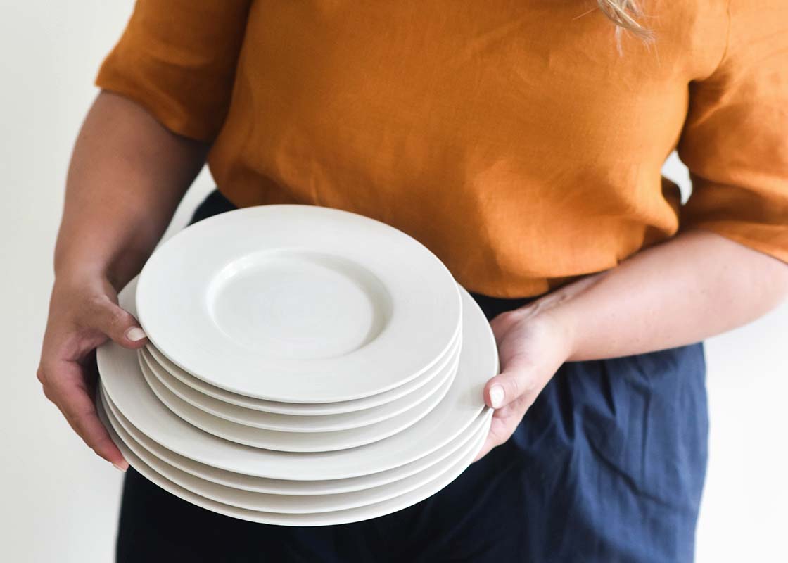 Cropped View of Woman holding Stack of Signature White Rimmed Dinner Plates