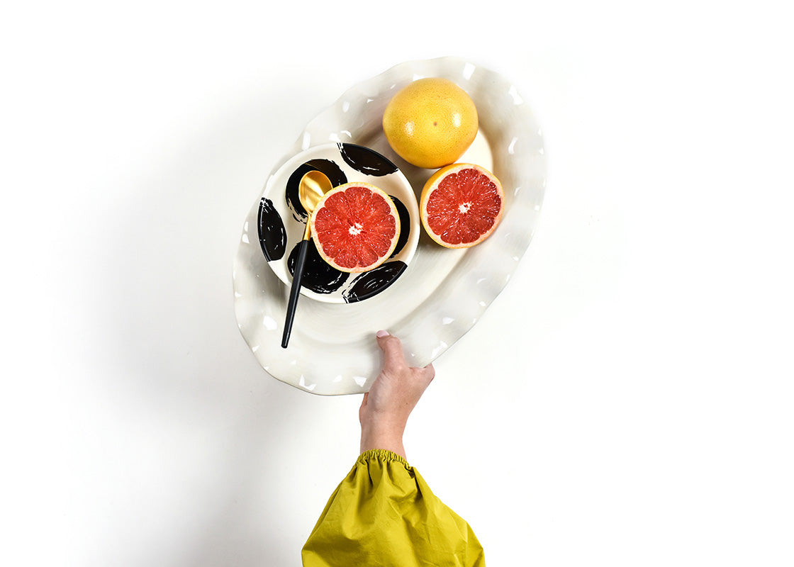 Overhead View of Hand Holding Signature White Platter and Brushed Dot Bowl with Sliced Grapefruit on Top