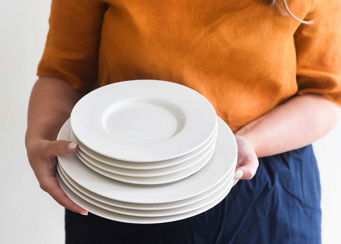 Front View of Woman Holding Stack of Dishes including Signature White Rimmed Salad Plate Set of 4 Tipped to See Top Plate