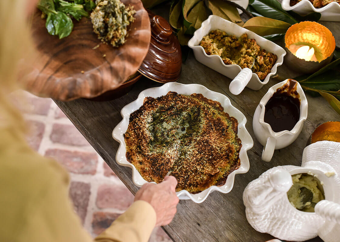 Overhead View of Woman Scooping Spinach from Signature White 9in Ruffle Pie Dish in Harvest Tablescape