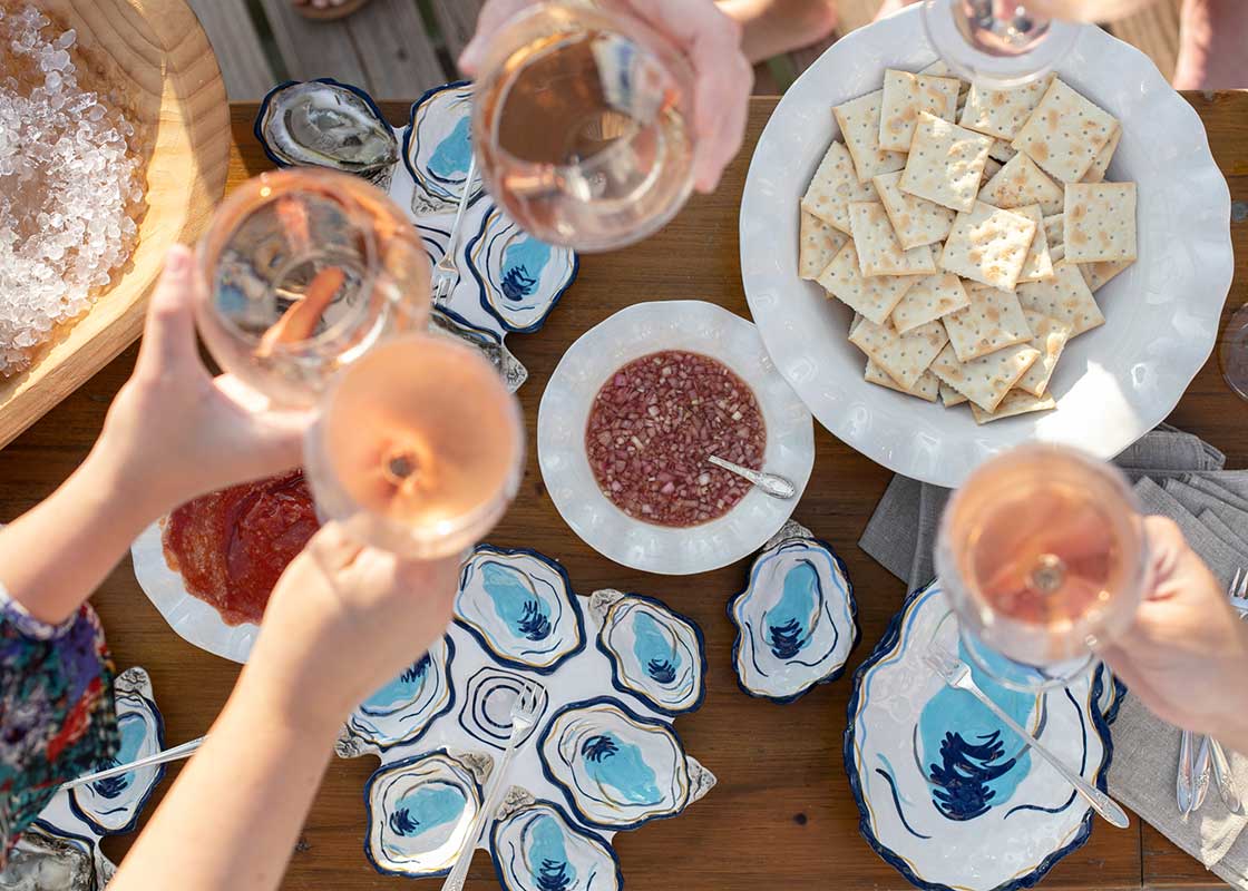 Overhead View of Hands raising wine glasses over a table of food. Tablescape Featuring Coton Colors Designs Including Ruffle Best Bowl in Signature White