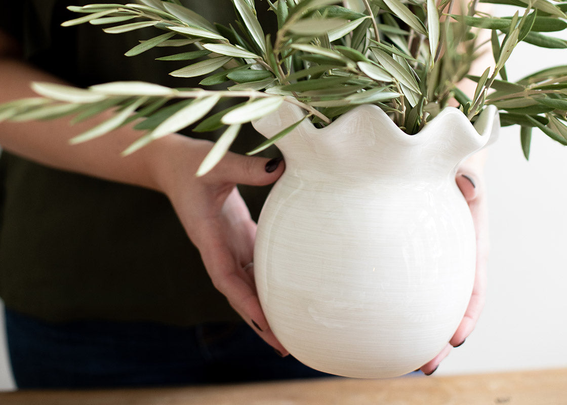 Close up of Person Holding Signature White Vase Filled with Olive Branches