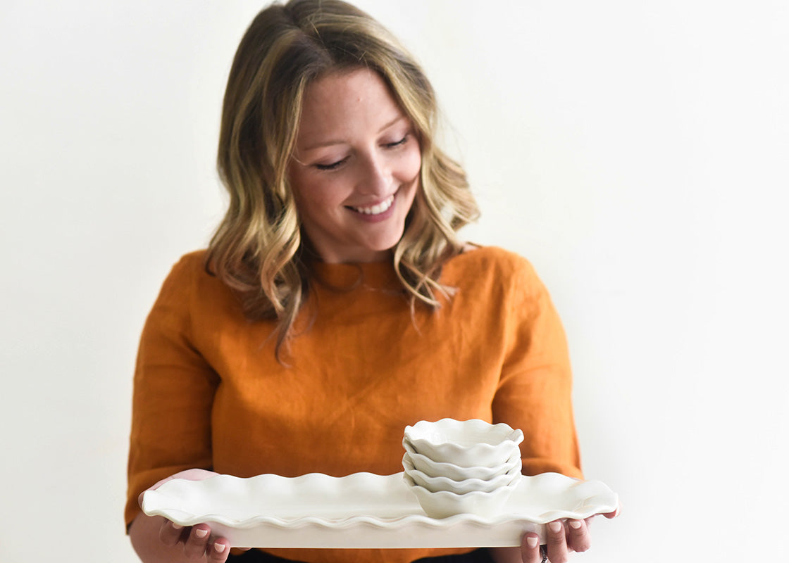 Front View of Woman Smiling and Holding a Ruffled Oval Tray with Dipping Bowls Stacked on top in Signature White Ruffle Design