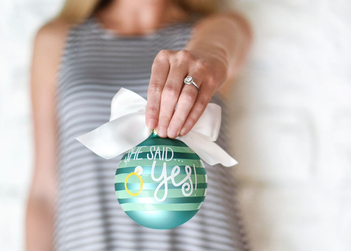 Front View of She Said Yes Just Engaged Glass Ornament Held by Woman with Engagement Ring